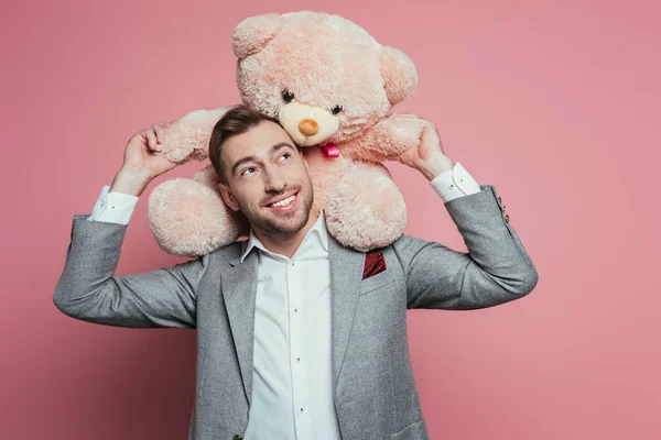 Позитивний бородатий чоловік у костюмі тримає плюшевого ведмедя на рожевому — стокове фото