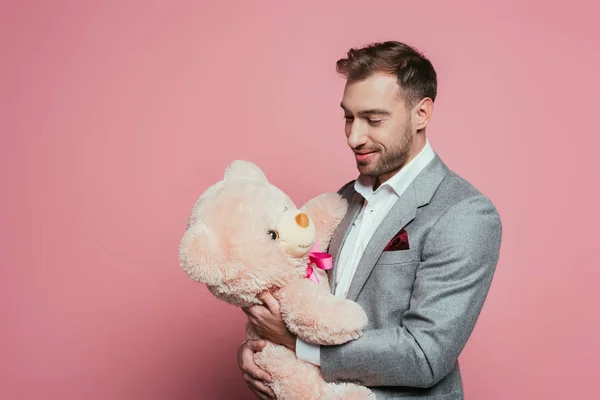 Homme souriant barbu en costume tenant ours en peluche, isolé sur rose — Photo de stock