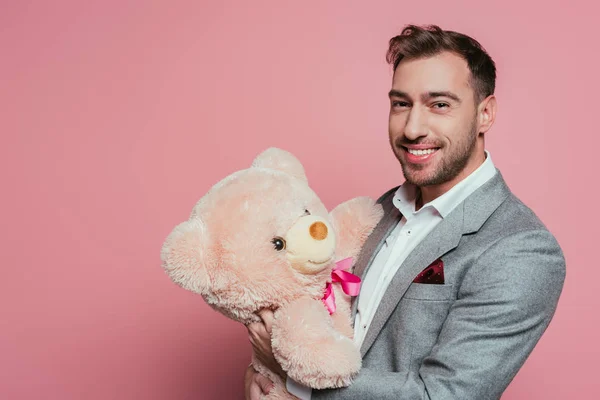 Бородатий чоловік у костюмі тримає плюшевого ведмедя, ізольований на рожевому — стокове фото
