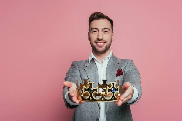 Sonriente hombre barbudo en traje sosteniendo corona, aislado en rosa - foto de stock