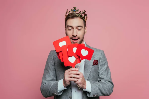 Homme heureux dans la couronne tenant des cartes avec des coeurs pour la Saint-Valentin, isolé sur rose — Photo de stock