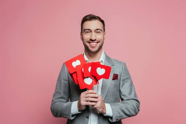 Uomo sorridente in possesso di carte con il cuore per San Valentino, isolato su rosa — Foto stock