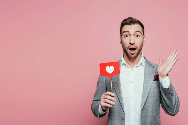 Homem surpreso segurando cartão com coração para o dia dos namorados, isolado no rosa — Fotografia de Stock