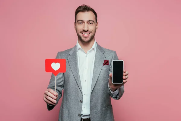 Homem feliz segurando smartphone com tela em branco e cartão com coração para o dia dos namorados, isolado no rosa — Fotografia de Stock