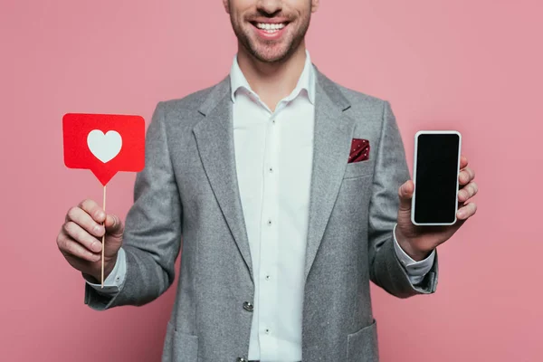 Vista recortada del hombre sosteniendo teléfono inteligente con pantalla en blanco y tarjeta con corazón para el día de San Valentín, aislado en rosa - foto de stock