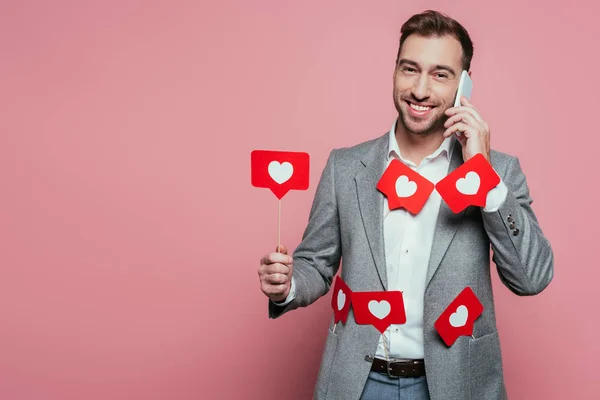 Uomo allegro che parla su smartphone e tiene carte con cuori per il giorno di San Valentino, isolato su rosa — Foto stock