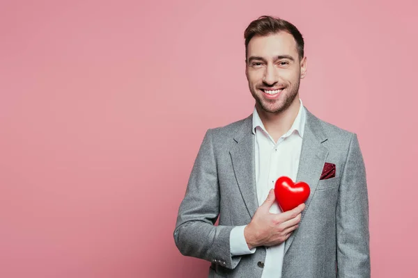 Felice uomo che tiene il cuore rosso per San Valentino, isolato su rosa — Foto stock