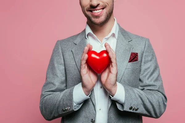 Abgeschnittene Ansicht eines lächelnden Mannes mit rotem Herz zum Valentinstag, isoliert auf rosa — Stockfoto