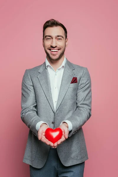 Bell'uomo allegro che tiene il cuore rosso per San Valentino, isolato sul rosa — Foto stock