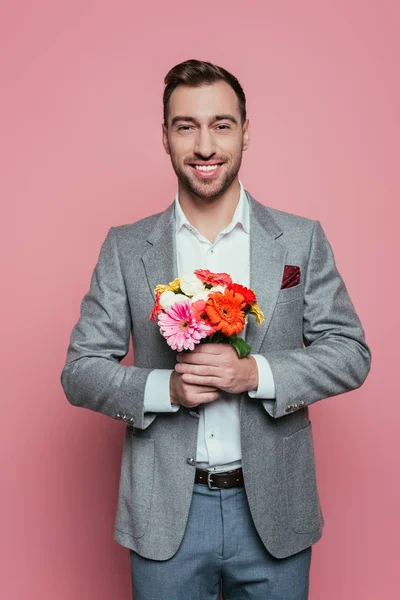 Uomo sorridente che tiene mazzo di fiori, isolato su rosa — Foto stock