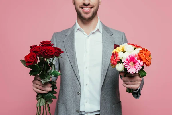Vista ritagliata di uomo felice in giacca e cravatta con due mazzi di fiori, isolato su rosa — Foto stock