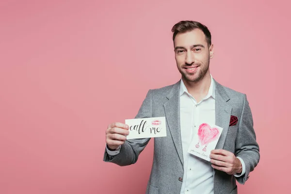 Hombre barbudo guapo sosteniendo dos tarjetas de San Valentín, aislado en rosa - foto de stock