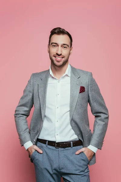 Homem positivo barbudo em terno cinza com as mãos nos bolsos, isolado em rosa — Fotografia de Stock