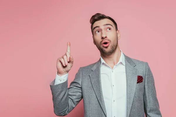 Excited handsome man in grey suit pointing up, isolated on pink — Stock Photo