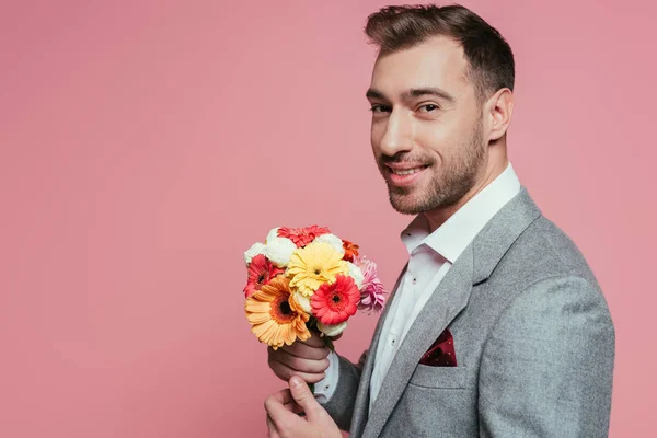 Hombre sonriente barbudo sosteniendo ramo de flores, aislado en rosa - foto de stock