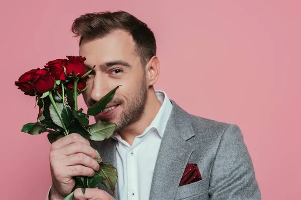 Cheerful man in suit holding red roses, isolated on pink — Stock Photo