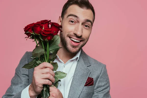 Animado bonito homem de terno segurando rosas, isolado em rosa — Fotografia de Stock