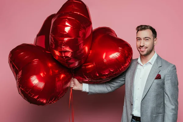 Homme heureux tenant ballons coeur rouge pour la Saint-Valentin sur rose — Photo de stock