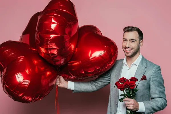 Emotional man holding roses and red heart balloons for valentines day on pink — Stock Photo