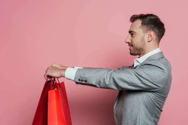 Hombre feliz sosteniendo bolsas de compras, aislado en rosa - foto de stock