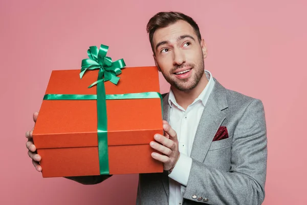 Sonriente hombre de traje sosteniendo gran caja de regalo, aislado en rosa - foto de stock