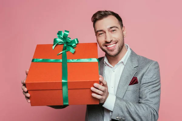 Hombre positivo en traje que sostiene la caja de regalo grande, aislado en rosa - foto de stock