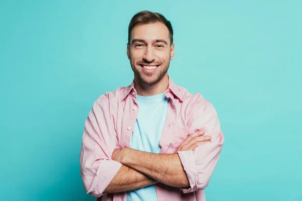 Hombre guapo sonriente con los brazos cruzados, aislado en azul - foto de stock