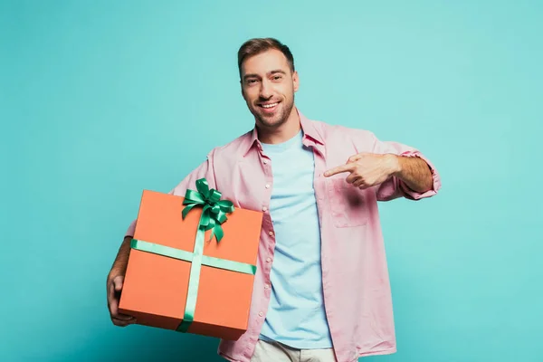 Homme souriant pointant vers grand coffret cadeau, isolé sur bleu — Photo de stock