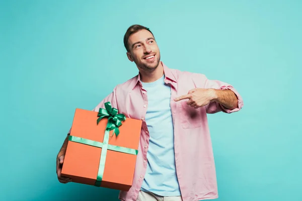 Hombre barbudo feliz apuntando a la caja de regalo grande, aislado en azul - foto de stock