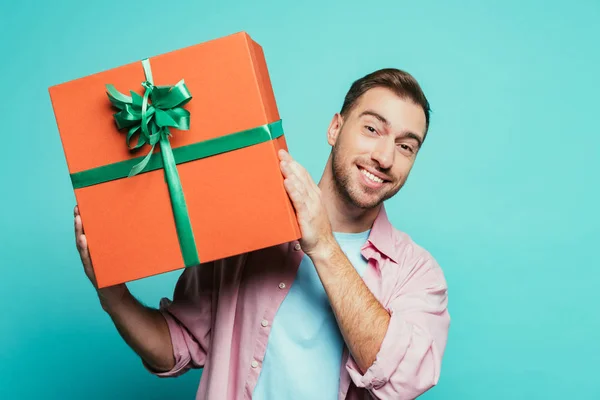 Улыбающийся мужчина держит большую подарочную коробку, изолированную на синий — стоковое фото