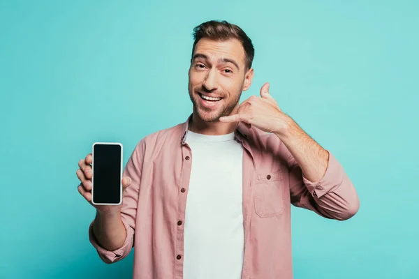 Fröhlich gutaussehender Mann zeigt Call Me Sign Smartphone mit leerem Bildschirm, isoliert auf blau — Stockfoto