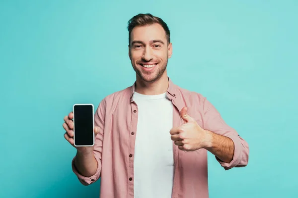 Homem alegre mostrando polegar para cima e smartphone com tela em branco, isolado em azul — Fotografia de Stock