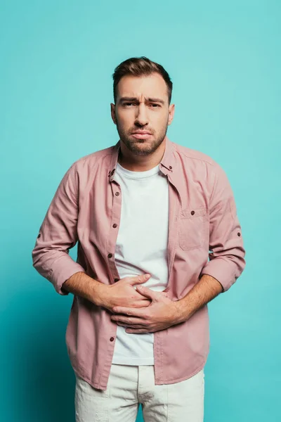 Verärgerter schöner Mann mit Bauchschmerzen, isoliert auf blauem Grund — Stockfoto