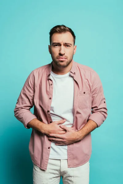 Chateado bonito homem ter dor de estômago, isolado em azul — Fotografia de Stock