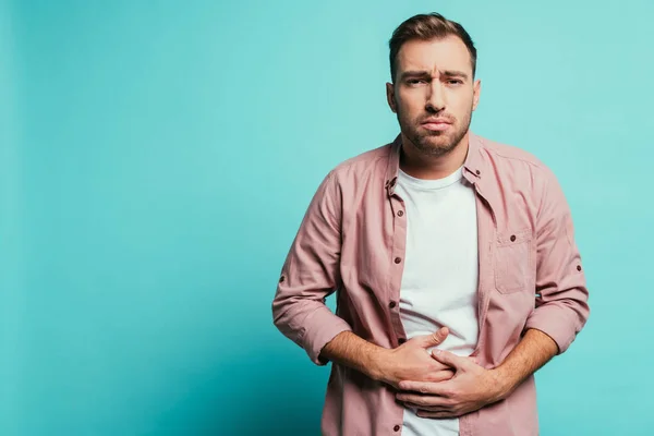 Upset handsome man having abdominal pain, isolated on blue — Stock Photo