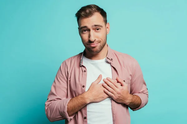 Alegre guapo hombre cogido de la mano en el corazón, aislado en azul - foto de stock