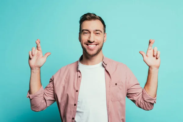 Cheerful handsome man with fingers crossed isolated on blue — Stock Photo