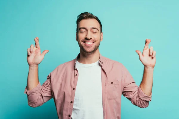 Homem alegre com olhos fechados e dedos cruzados isolado em azul — Fotografia de Stock