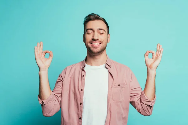 Hombre alegre con los ojos cerrados mostrando om gesto, aislado en azul - foto de stock