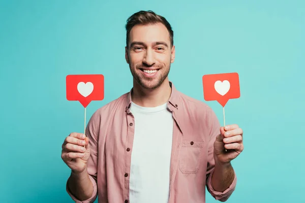 Sonriente hombre sosteniendo tarjetas con corazones para el día de San Valentín, aislado en azul - foto de stock