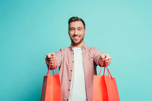 Sonriente hombre sosteniendo bolsas de compras, aislado en azul - foto de stock