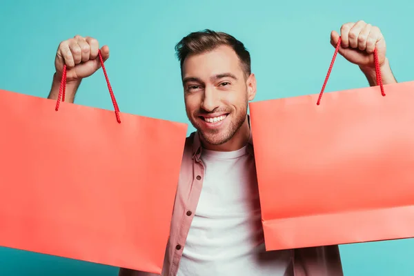 Cheerful man holding shopping bags, isolated on blue — Stock Photo