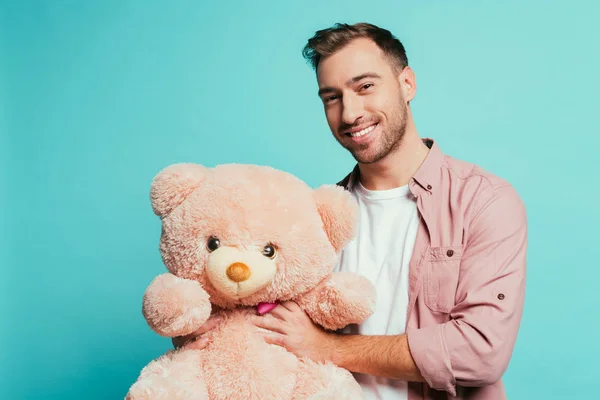 Cheerful bearded man holding teddy bear, isolated on blue — Stock Photo