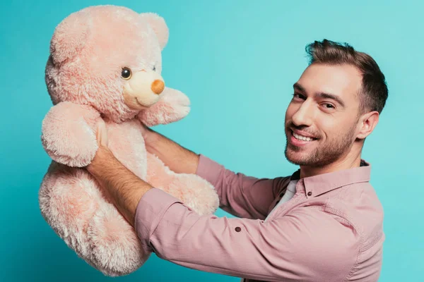 Бородатий усміхнений чоловік тримає плюшевого ведмедя, ізольований на синьому — стокове фото