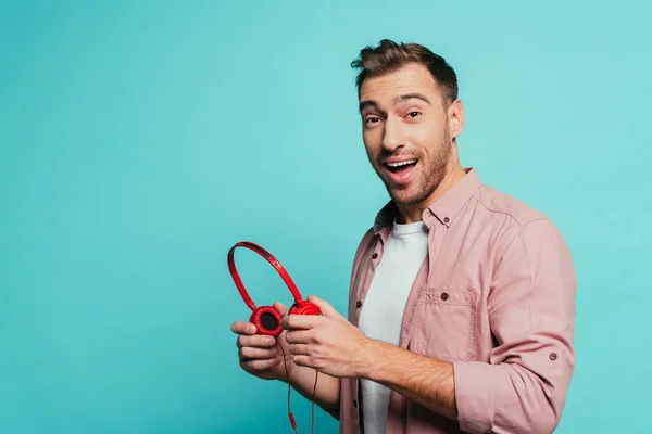 Excited man holding headphones, isolated on blue — Stock Photo