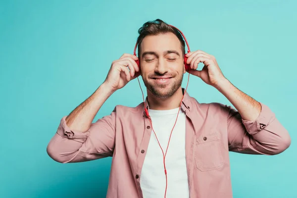 Hombre barbudo feliz escuchando música con auriculares, aislado en azul - foto de stock