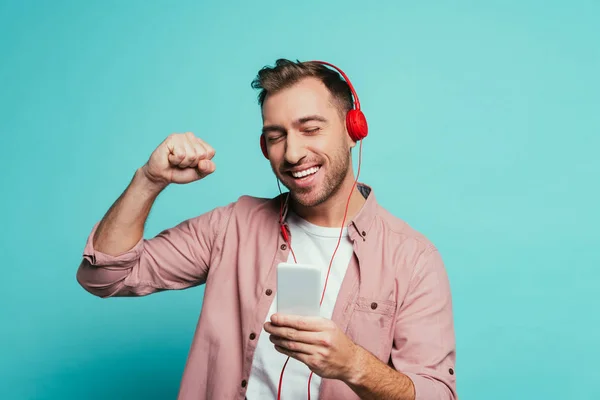 Веселий чоловік танцює і слухає музику з навушниками та смартфонами, ізольований на синьому — стокове фото