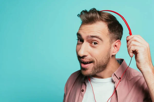 Hombre barbudo positivo escuchando música con auriculares, aislado en azul - foto de stock