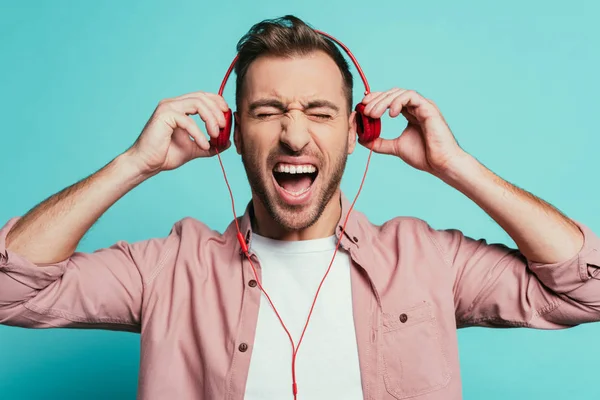 Hombre emocionado gritando y escuchando música con auriculares, aislado en azul - foto de stock