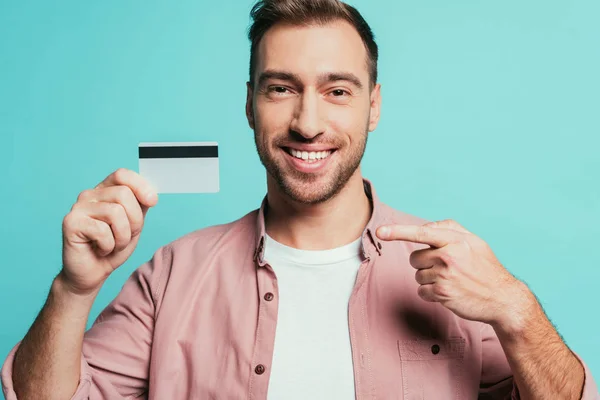 Homem barbudo feliz apontando para o cartão de crédito, isolado em azul — Fotografia de Stock